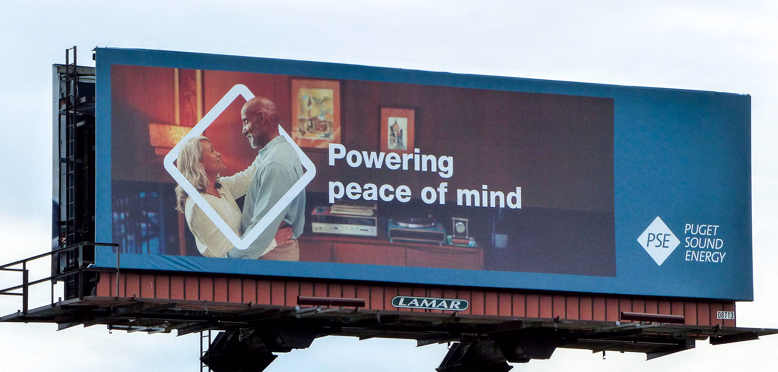 Outdoor billboard with PSE ad of elerly couple dancing. Headline: Powering peace of mind