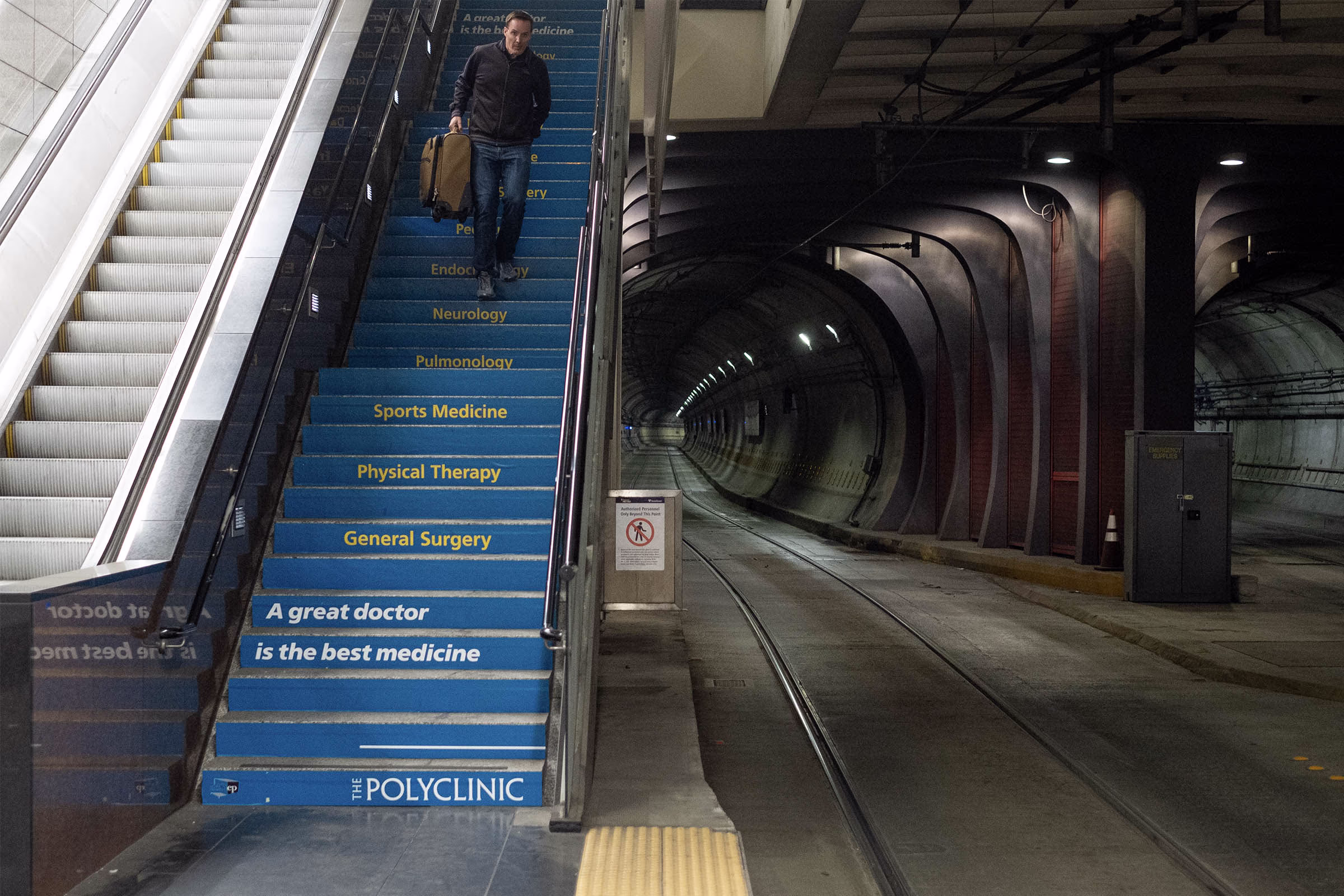Man descends subway stairs with The Polyclinic ad promoting sports medicine and physical therapy services.
